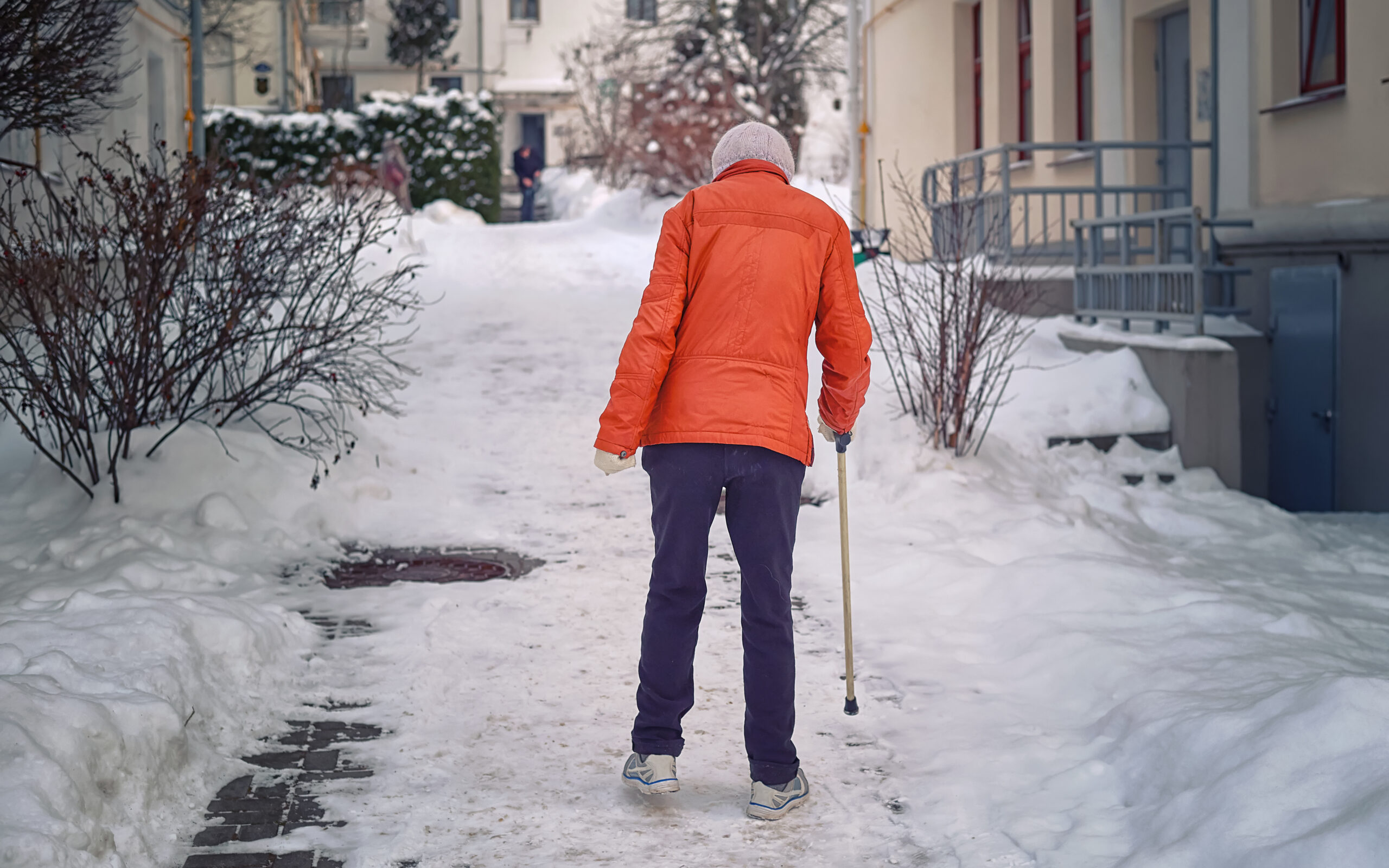 Disabled woman walks with stick after snowfall. Lame woman, disability and injury concept. Old woman with cane walking along slippery sidewalk in winter. Grandma with stick walking along snowy street